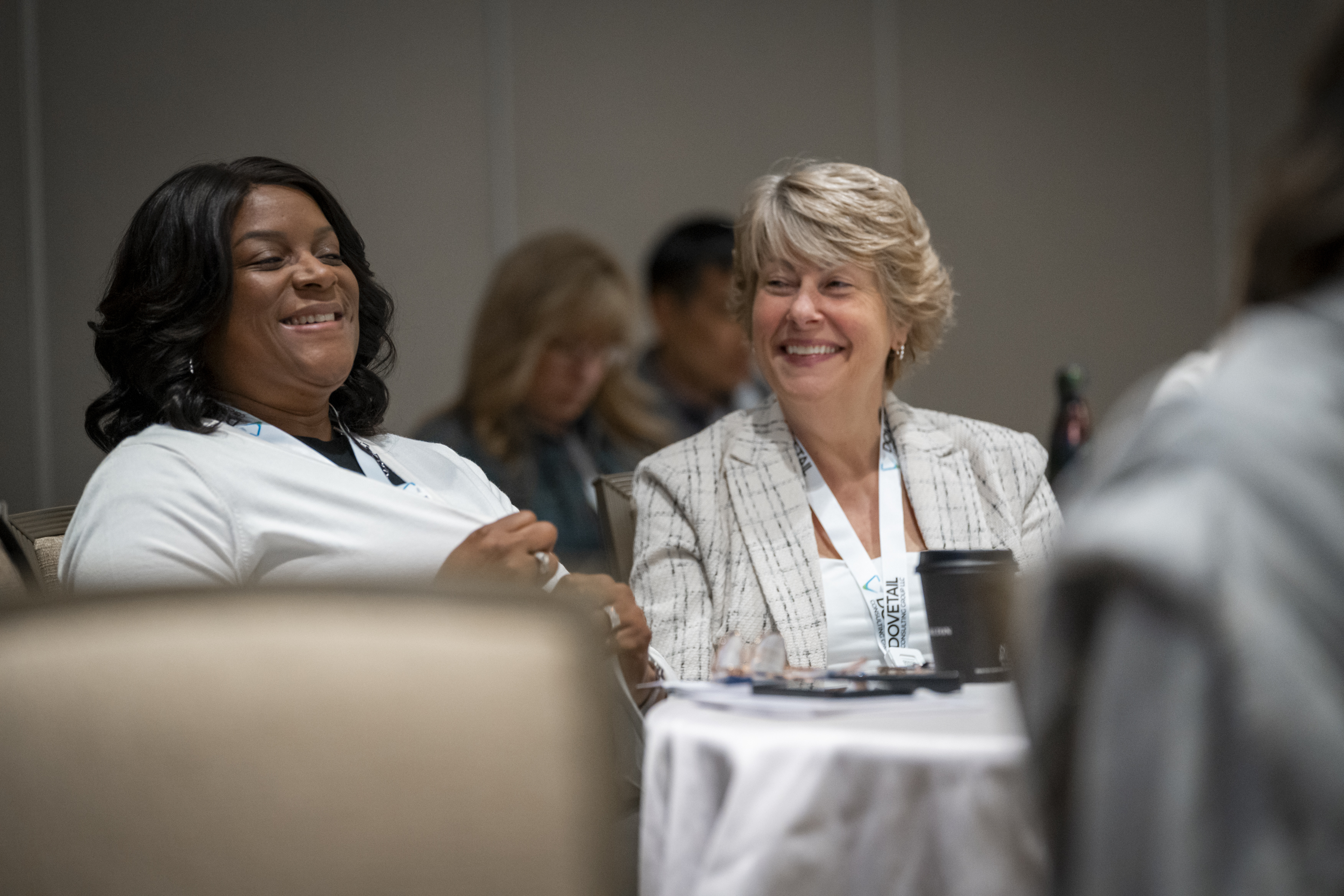 Two attendees sit by a table and laugh.