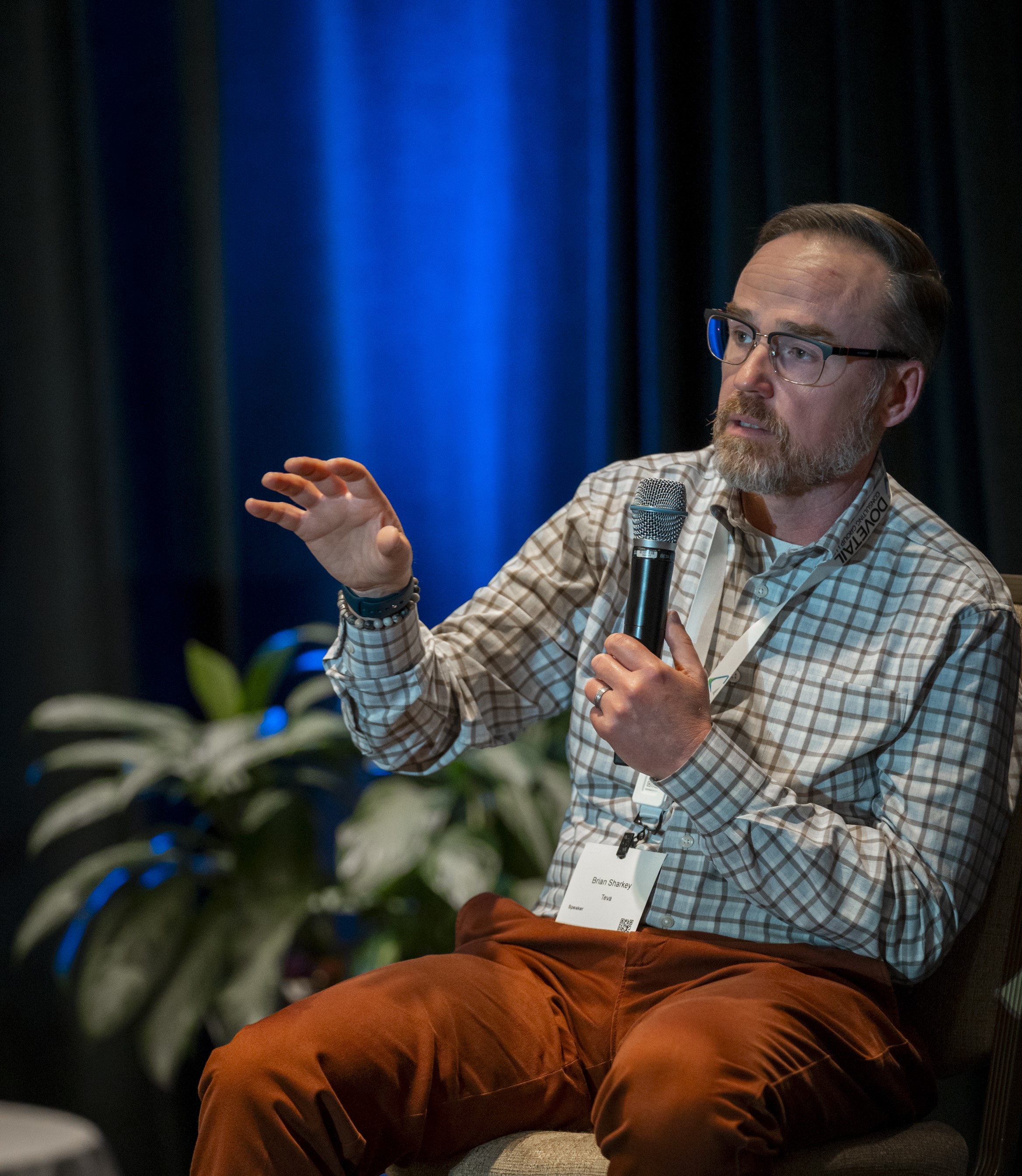 A speaker sits on stage and talks into a microphone.