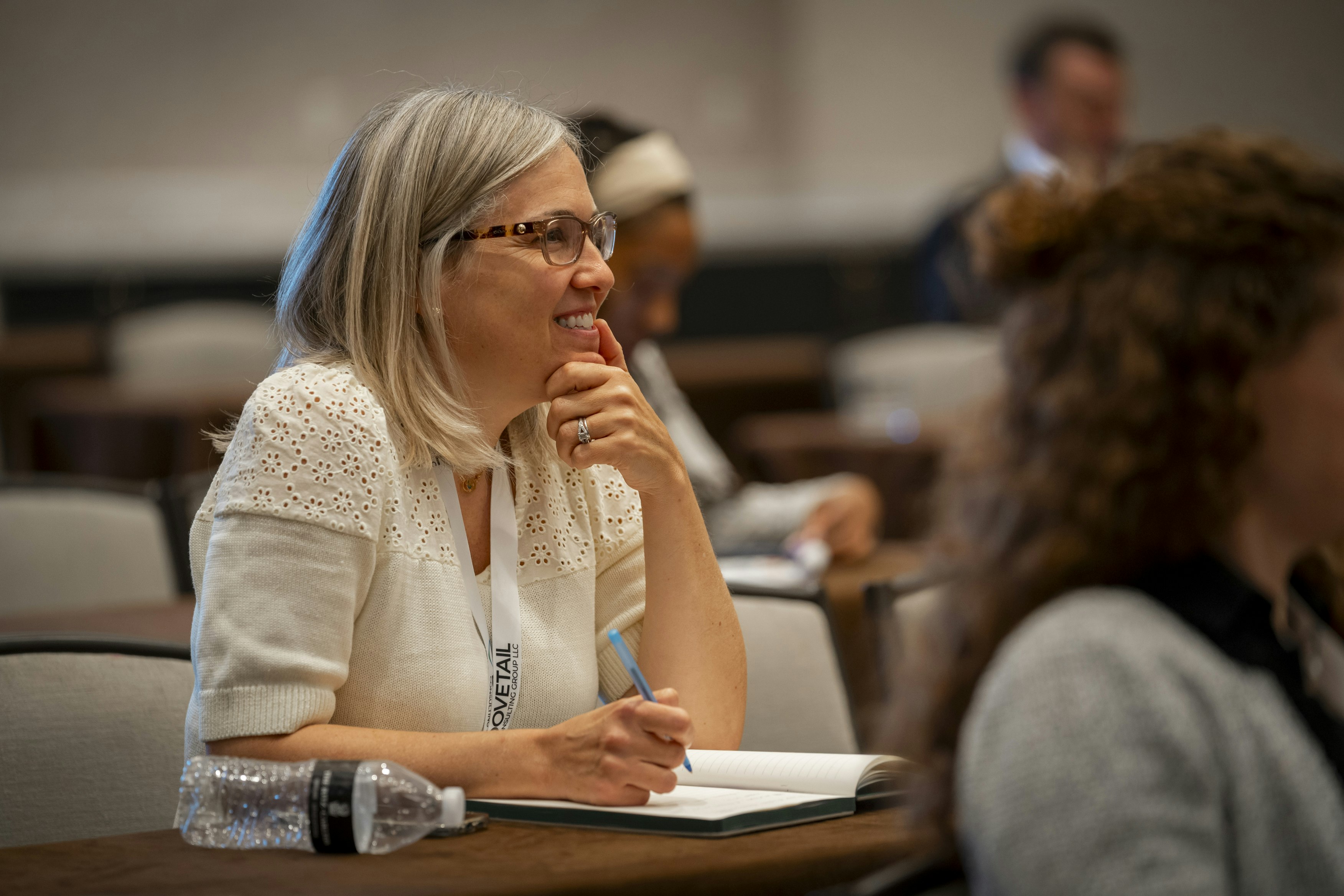 A woman smiles as she takes notes at Transparency & HCP Engagement conference with a pen and notebook.