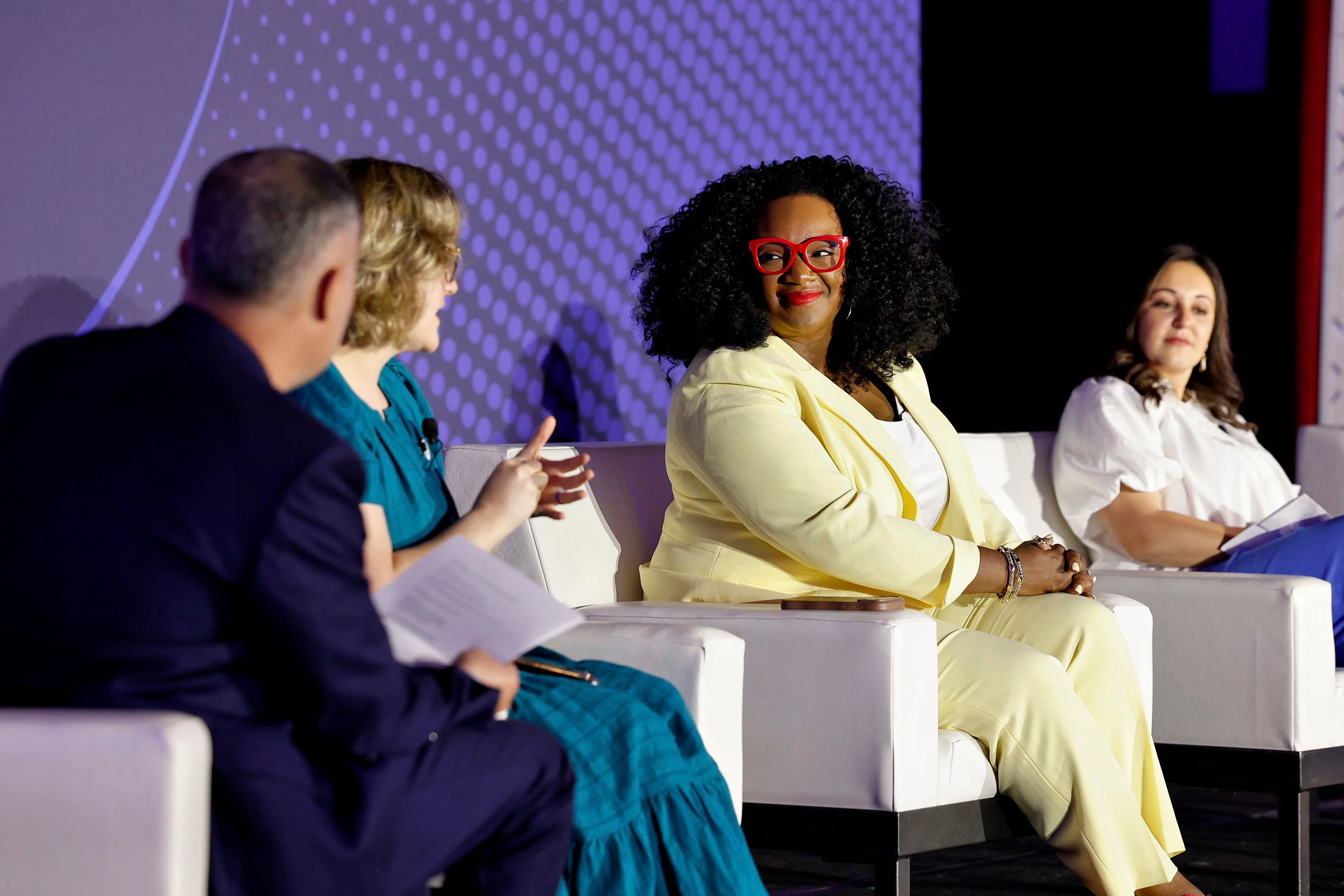 Two women accepting an eTSY Award. The woman on the left has dark curly hair and is wearing a black shirt with grey jeans. The woman on the right has straight blonde hair and is wearing a white blouse, black pants, and an Apple Watch.