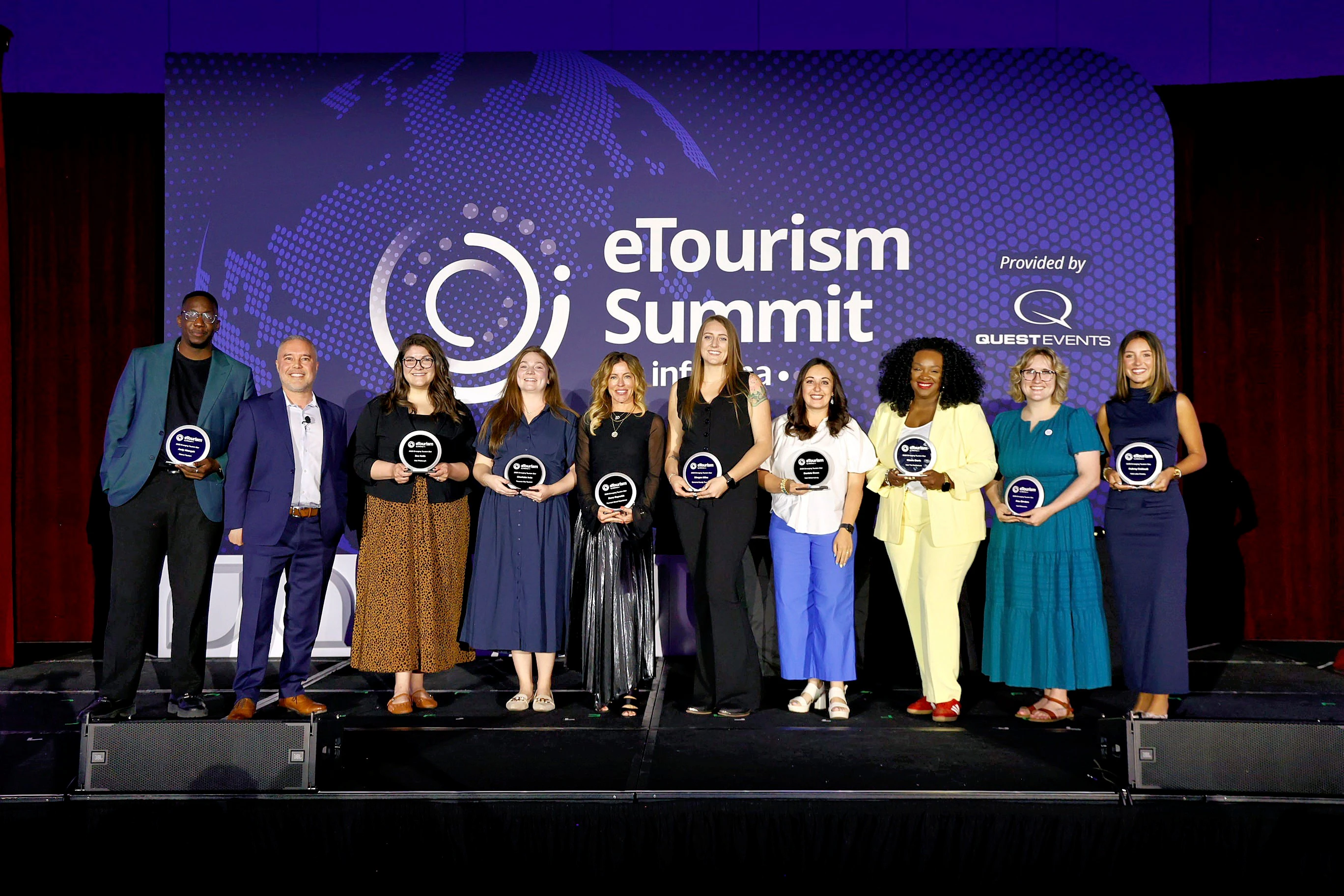 A group of professionals on stage at eTourism Summit smiling and holding their eTSY Awards.