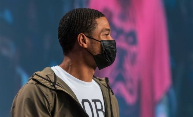 Ray Fisher stands in a green jacket with a black mask on