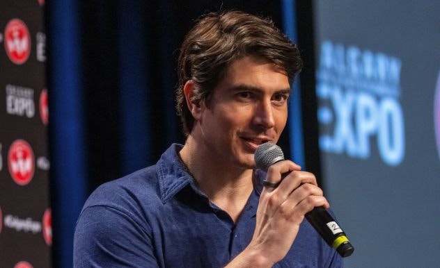 Brandon Routh holds a microphone up as he speaks on stage