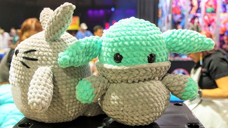 A knit grogu plushie and a todoro plushie are placed on top of a vendor's table