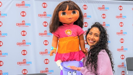 The voice of Dora holds up a Dora The Explorer doll