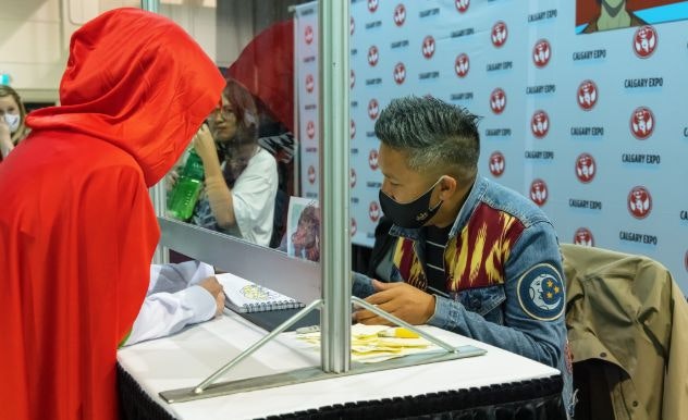 Dante Basco, wearing a Firebender jean jacket, signs an autograph wearing a black mask