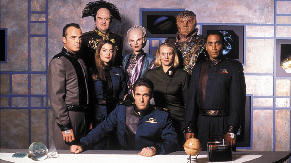 A photo of several cast members of Babylon 5, all dressed up in their character's outfits. At the back row, from left to right (actor's name) are Vir Cotto (Stephen Furst) & G'Kar (Andreas Katsulas). In the middle row are Michael Garibaldi (Jerry Doyle), Susan Ivanova (Claudia Christian), Delenn (Mira Furlan), Talia Winters (Andrea Thompson), & Stephen Franklin (Richard Biggs). At the bottom is Jeffrey Sinclair (Michael O'Hare).