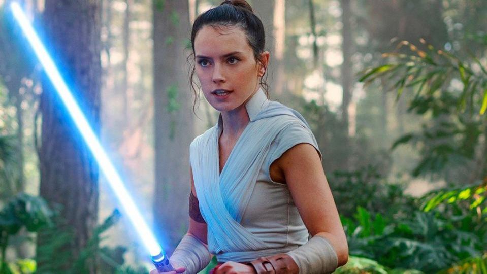 Rey from Star Wars holding her blue Lightsaber in the forest