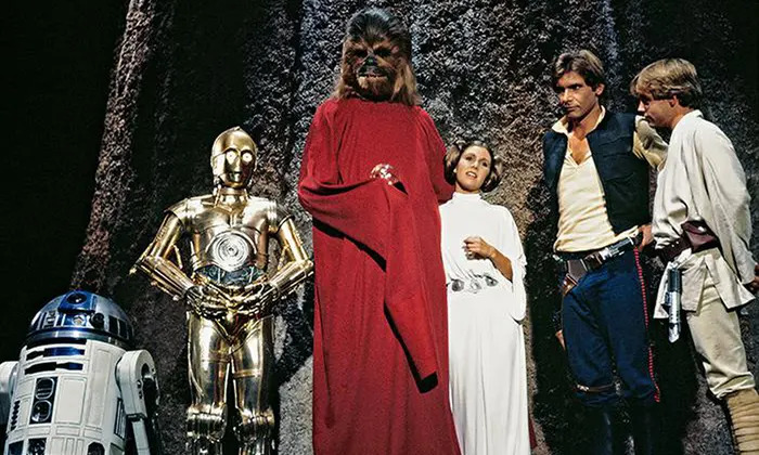 Some of the "stars" of the Star Wars Holiday Special, posing together in a shot. From left to right: R2-D2, C3-PO, Chewbacca, Leia Organa (Carrie Fisher), Han Solo (Harrison Ford), and Luke Skywalker (Mark Hamill).