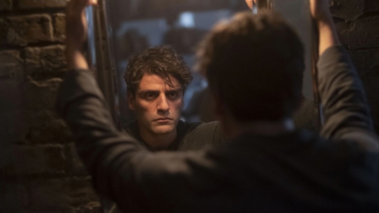 Steven Grant (Moon Knight) looking in the mirror very seriously with his arms extending above his head