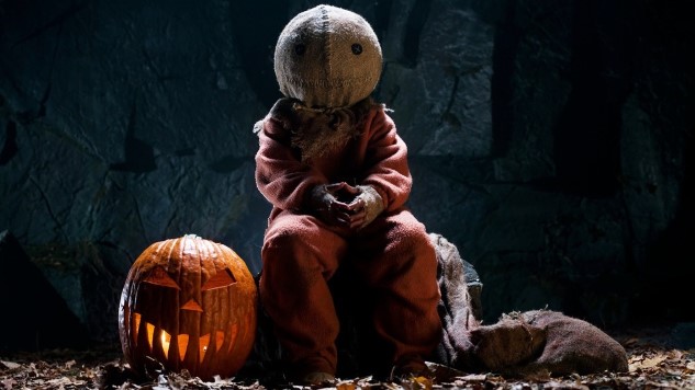 Sam, the antagonist of Trick 'r Treat, sitting beside a lit Jack-o-Lantern.