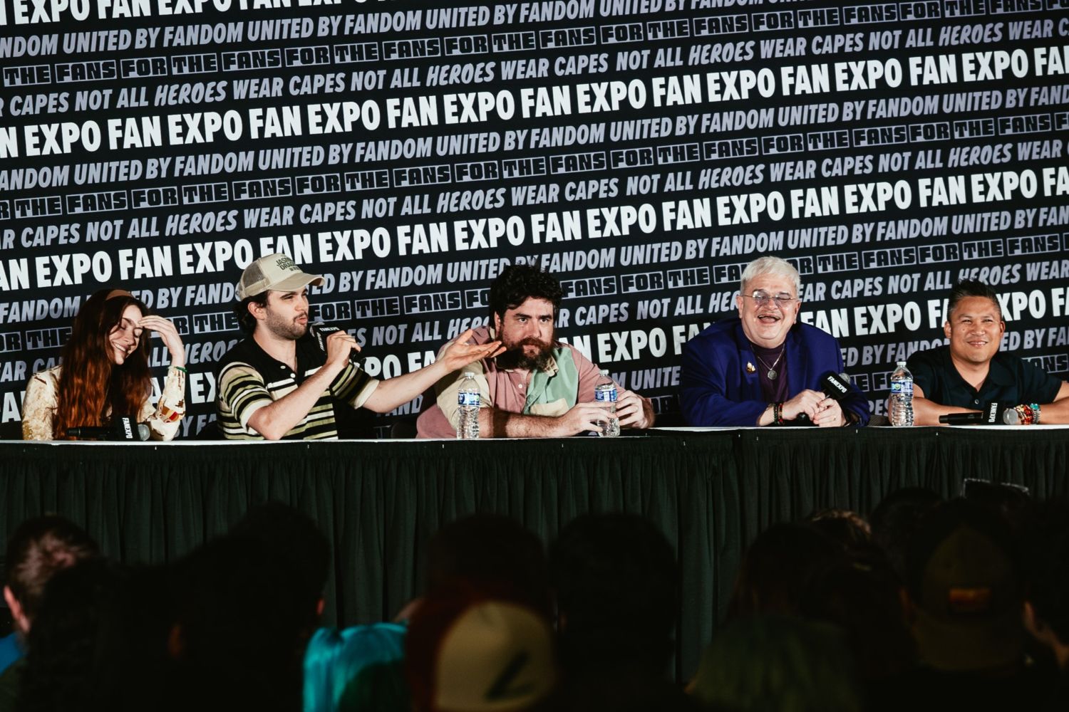 A group of five voice actors from Avatar: The Last Airbender sit at a long table, engaging with the audience. The panel, from left to right, includes Michaela Jill Murphy, Zach Tyler Eisen, Jack De Sena, Greg Baldwin, and Dante Basco, smiling and gesturing expressively, with water bottles and microphones in front of them.