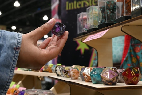 A hand holding a purple dice with many dice sitting on a display