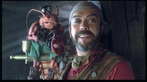 Long John Silver smiles in conversation. On his shoulder is a lobster muppet, listening intently.