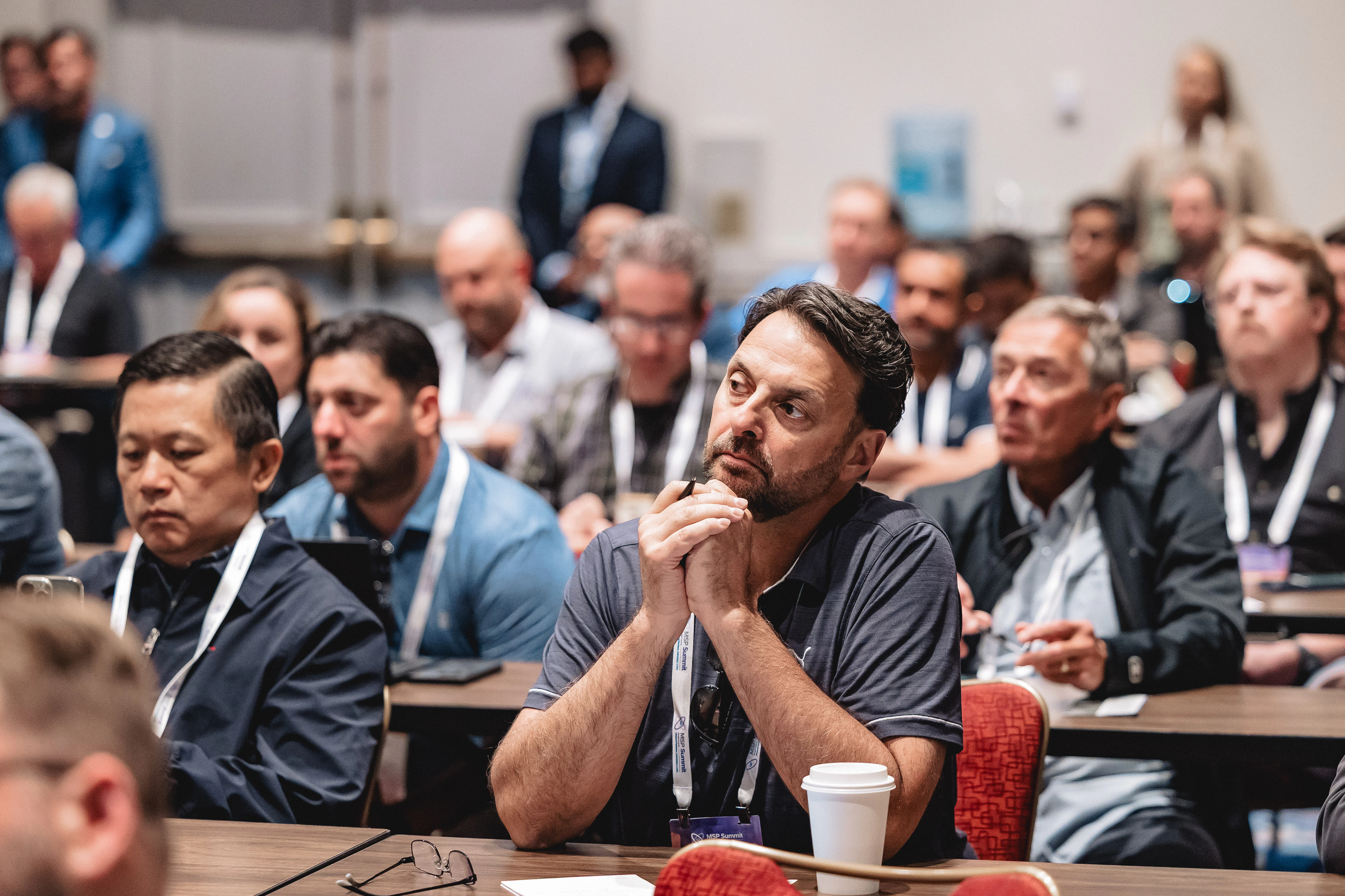 A man sits in a crowded audience listening to a session at MSP Summit.