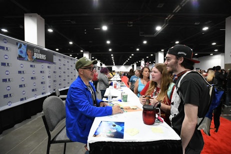 Steve Burns converses with two eager and excited fans at his signing table, crowds wait eagerly behind them to meet other celebrities