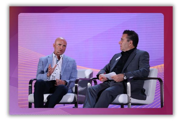 A photo of two men speaking onstage