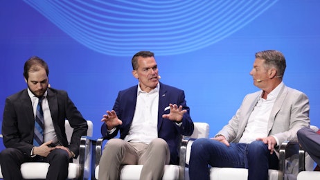 A photo of three men speaking onstage