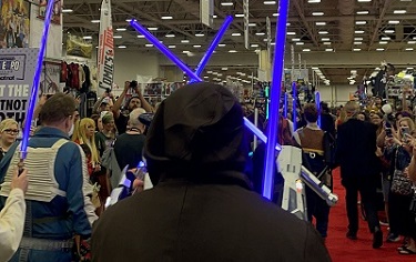 people cosplaying as star wars characters, holding up lightsabers and marching through the show floor