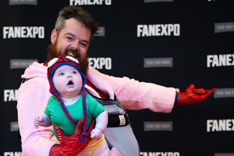 Spider-Man cosplayer holding a baby also dressed as Spider-Man