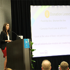 Conference speaker in front of a podium speaking about her slides on the projector
