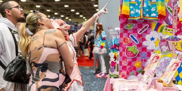 A young fan eagerly points at a bright and whimsical vendor booth, showing their parents an item.