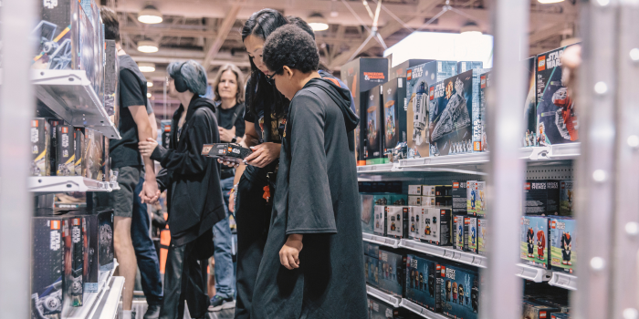 A mother and child check out a Lego set, standing amongst the aisle filled with new and available Lego set. 