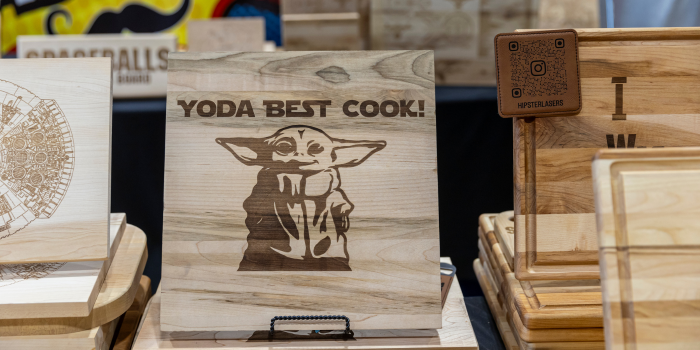 A selection of wooden cutting boards. The dominant board in the image has an engraving of Grogu and reads "YODA BEST COOK"