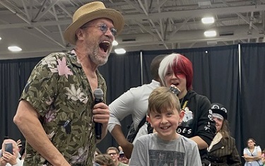 Michael Rooker holding a microphone, laughing next to a young boy, who is smiling