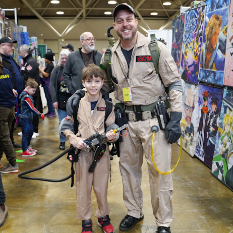 A father and son duo pose on the show floor in their ghostbusters suits.