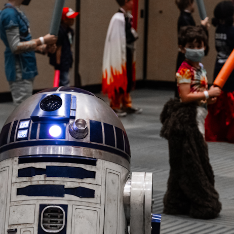 R2D2 in the foreground with jedi younglings practicing in the background