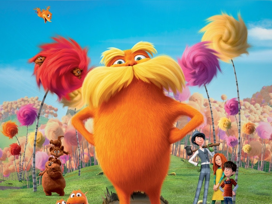 The Lorax stands proudly in front of a selection of truffula trees. to his left, the bears are doing tricks, and right, Ted, Audrey, and the Onceler smile toward the screen