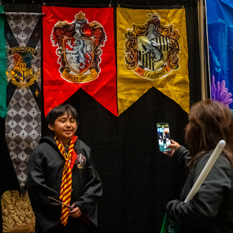Kid dressed in Gryffindor robes posing for a pic in front of the Hogwarts House banner