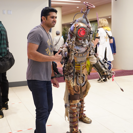 A fan poses for a photo with a Bioshock cosplayer. The cosplayer is in a diving suit, and the fan is in a grey tshirt and blue jeans.