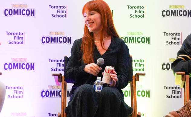Ruth Connell smiles to a person off camera. In one hand, she holds her microphone, the other holding a diet coke.