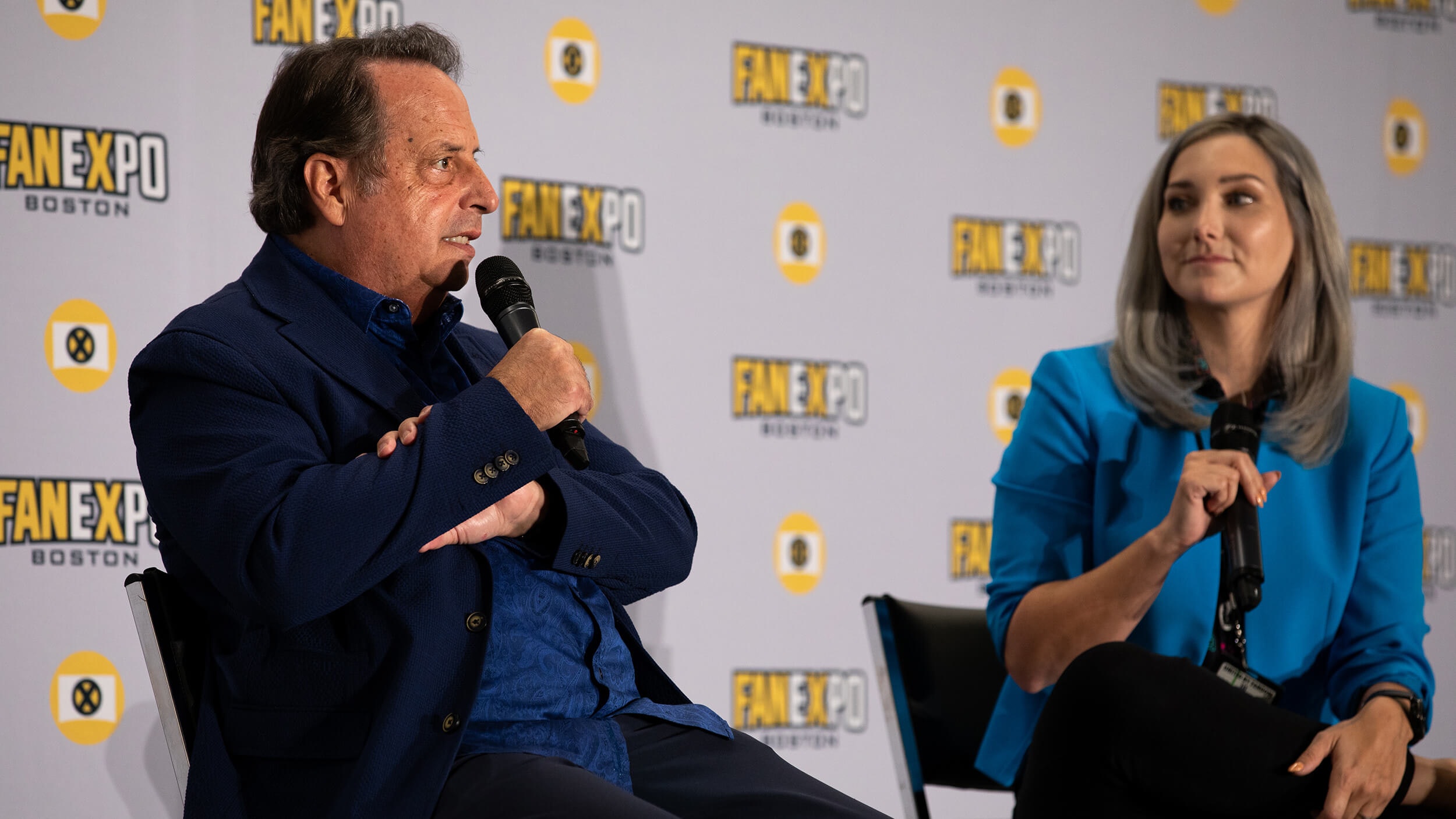 Jon Lovitz speaks on stage with a microphone in his hands