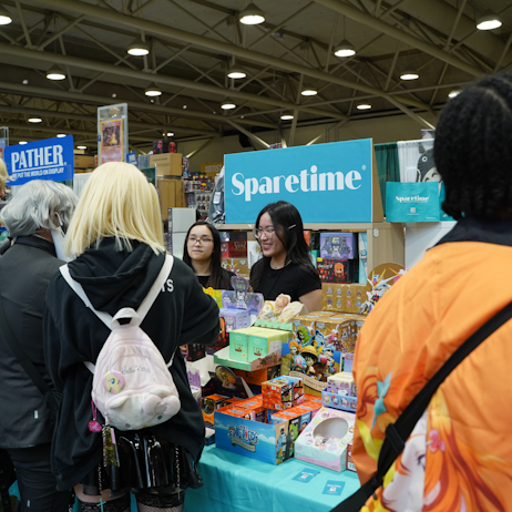 The team at Sparetime greets shoppers. Their bright blue sign sitting behind them, with blind box options on the table between them and the fans.