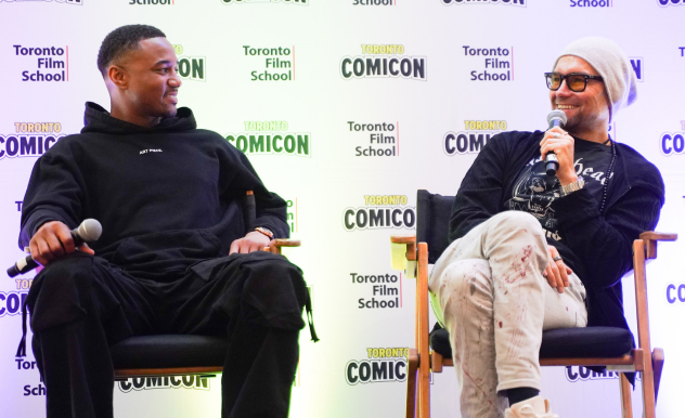 The Boys stars Jessie T. Usher (left) and Antony Starr (right) are seated in directors chairs answering questions during their Q+A. Both smile as Antony speaks. 