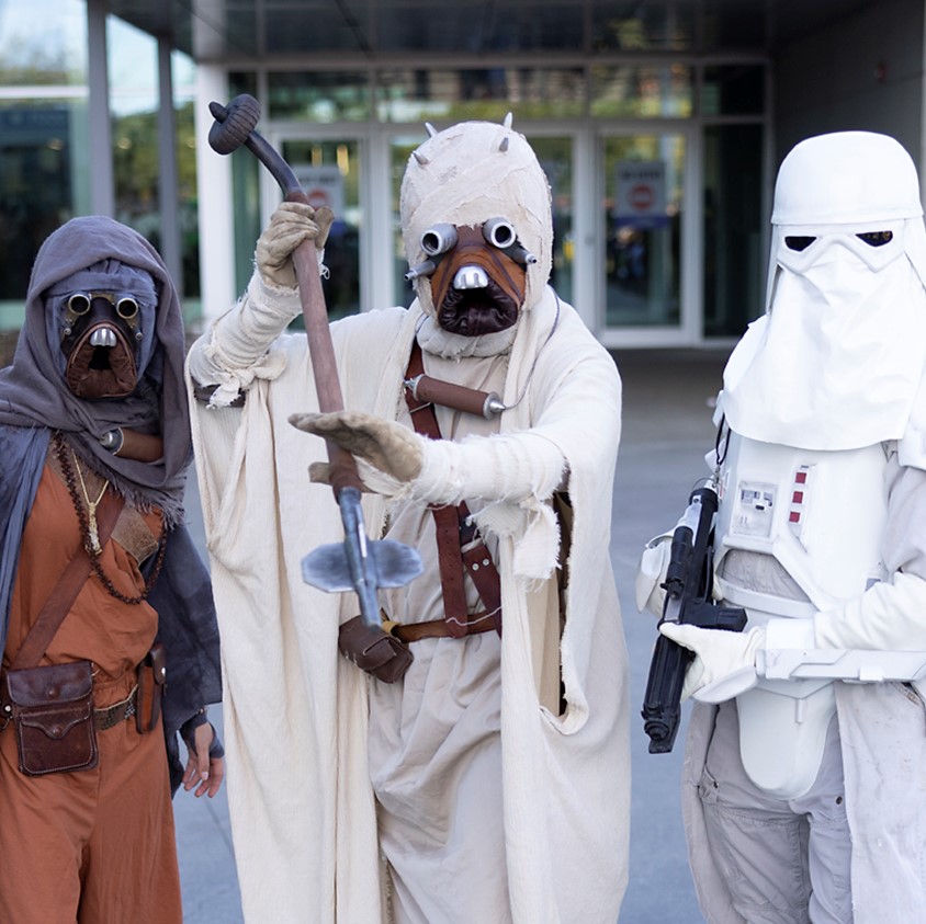 Two Tusken Raider cosplayers pose with a Stormtrooper Cosplayer