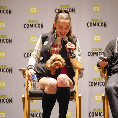 Christina Chong smiles as she introduces her puppy pal, Runa, to the audience. Runa is a small, brown, poodle.