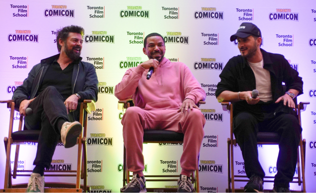 (L-R) The Boys stars Karl Urban, Laz Alonso, and Tomer Capone are seated in director's chairs, all three smile as they address the audience off screen.