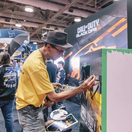 A pair of professional artists paint the cover are for Call of Duty Black Ops 6. They work on separate parts of the piece and are heavily focused. 