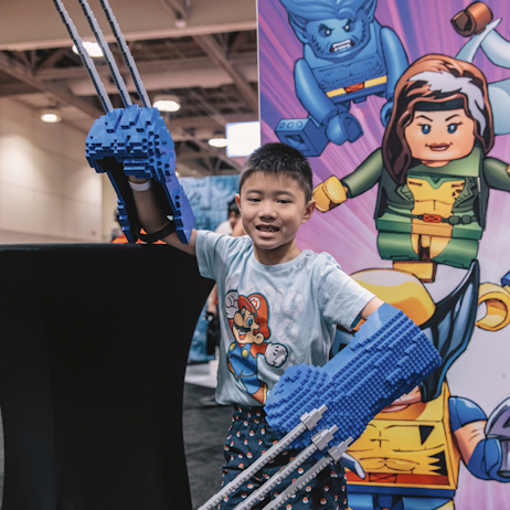 A child in a Mario t-shirt poses holding large blue and grey Wolverine talons.