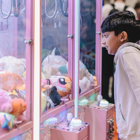 A young child eagerly approaches the large pink clow machine full of stuffed Powerpuff Girls.