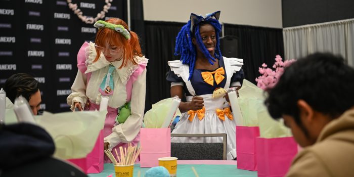 Two people dressed as maids for a maid cafe. One is smiling at the guests and one is pouring a drink.