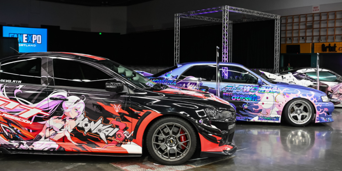 Itasha car display. Picture features a black car with pink -haired anime character decal on side.
