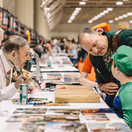 John Rhys-Davies holds the axe of a young man and his family. He is discussing the item with the child and father and eagerly listens as the child speaks. 
