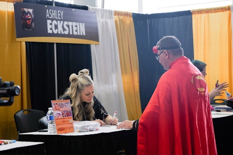 Ashley Eckstein focuses on signing an autograph for a fan dressed as Superman
