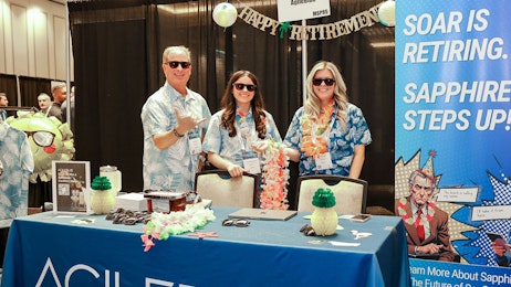 A photo of a man and two women dressed in Hawaiian shirts and leis in a trade show booth