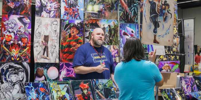 Artist stands before colorful print selection chatting with a customer